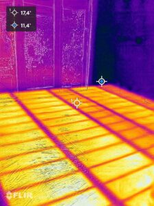 De afbeelding toont een thermische foto van een vloer en een glazen wand. De temperatuurmetingen zijn 17,4°C en 11,4°C. Schaduwpatronen zijn zichtbaar op de vloer.